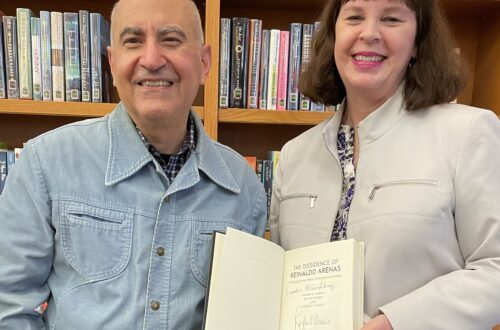 Professor Rafael Ocasio and director of library services Liz Bagley stand with an open book in front of a bookshelf.