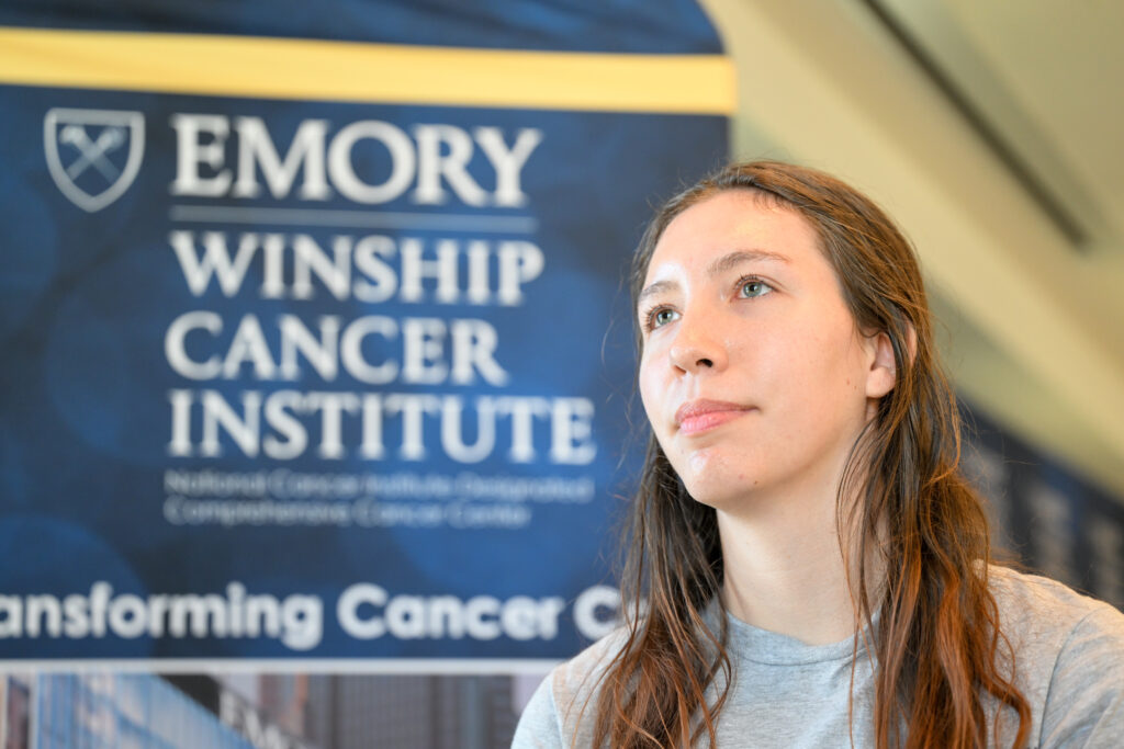 A student stands in the foreground off the the right. A banner with the words Emory Winship Cancer Institute is in the background.