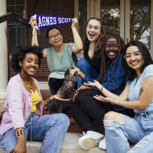 students sit on stairs next to Scottie dog statue and holding Agnes Scott purple pennants