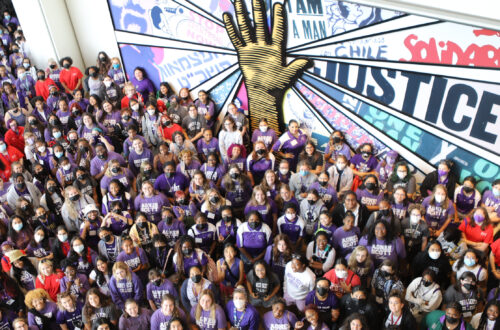 a large group of students wearing purple shirts stand in front of a wall mural encouraging justice