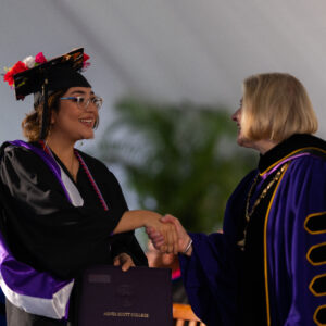 A graduate in their regalia shaking hands with President Zak.
