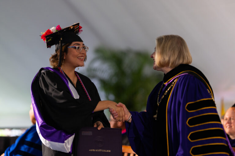 A graduate in their regalia shaking hands with President Zak.