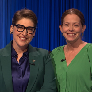 Two women wearing green clothing stand side-by-side while wearing lapel microphones