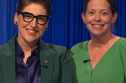 Two women wearing green clothing stand side-by-side while wearing lapel microphones