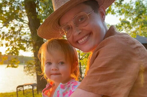 A women with a brimmed hat smiles in the light of a sunset while holding a young child.