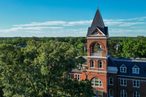 a drone photo of a historic building rises up among a crop of trees