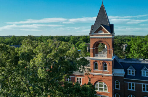 a drone photo of a historic building rises up among a crop of trees