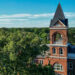 a drone photo of a historic building rises up among a crop of trees
