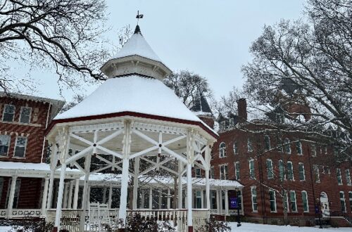 a photo of a gazebo in the snow with an academic building in the background
