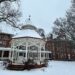 a photo of a gazebo in the snow with an academic building in the background